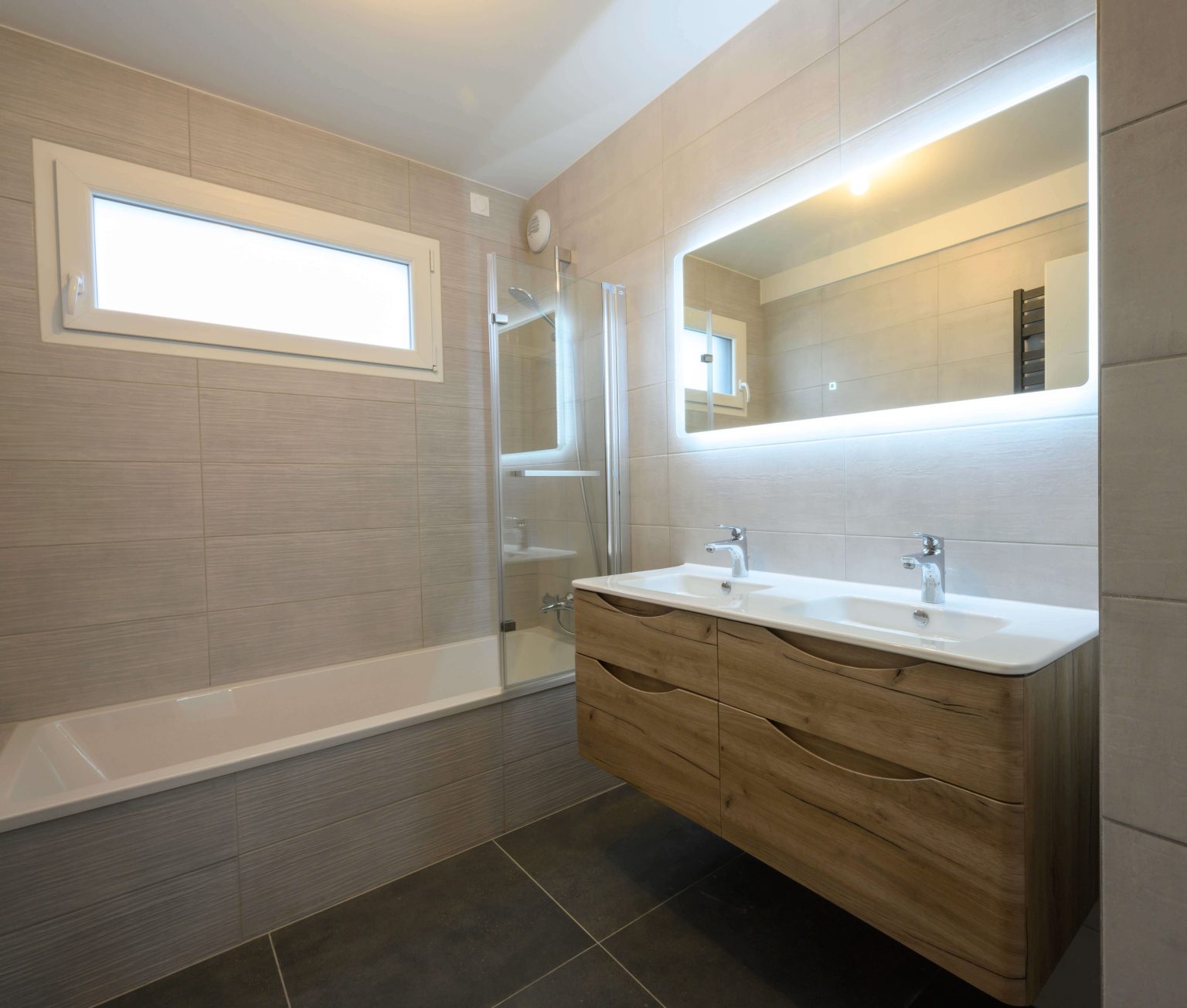 Grande salle de bain lumineuse avec doubles vasques, baignoire et miroir lumineux